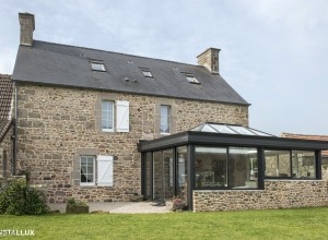 Véranda aluminium à toiture vitrée adossée à une maison en pierre