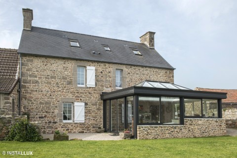 Véranda aluminium à toiture vitrée adossée à une maison en pierre